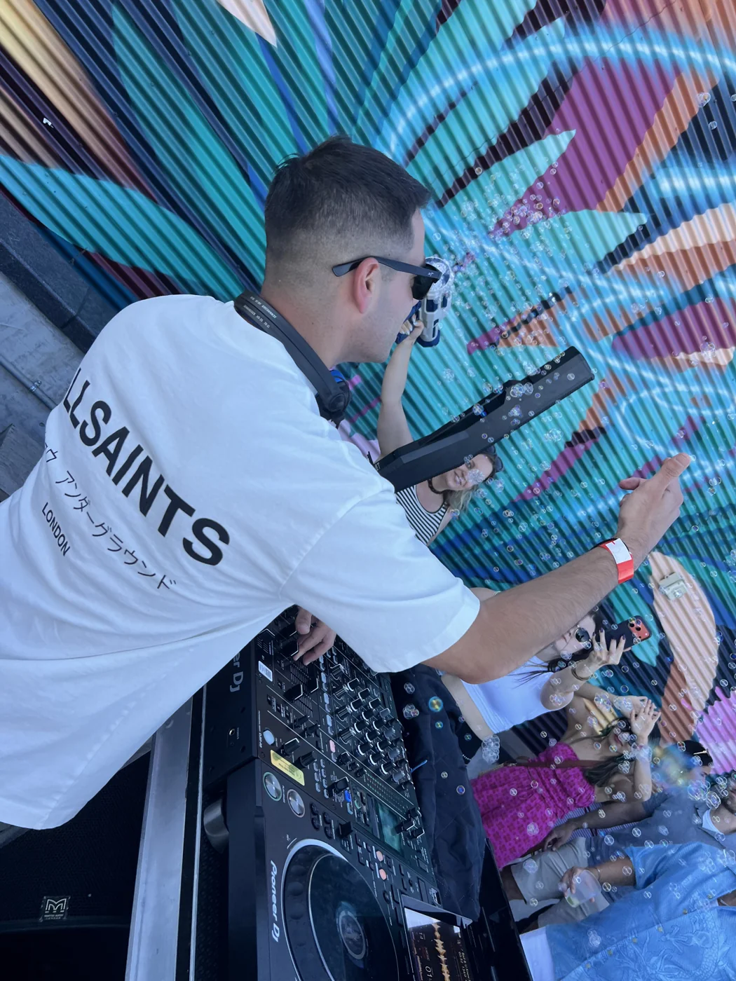 Andrew Weiss lifting his arm toward the crowd from the DJ booth
