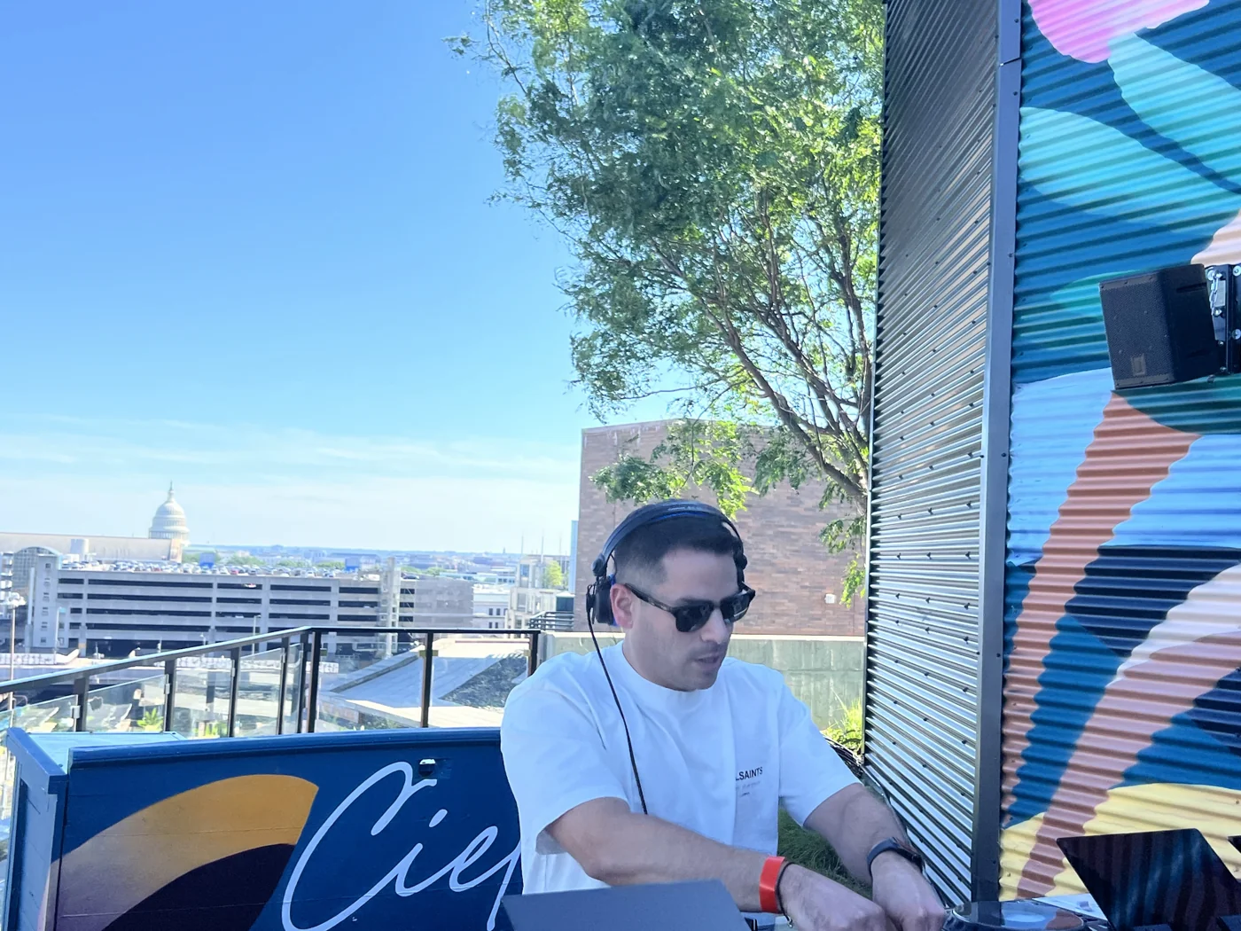 Andrew Weiss mixing on the decks beside a colorful rooftop mural